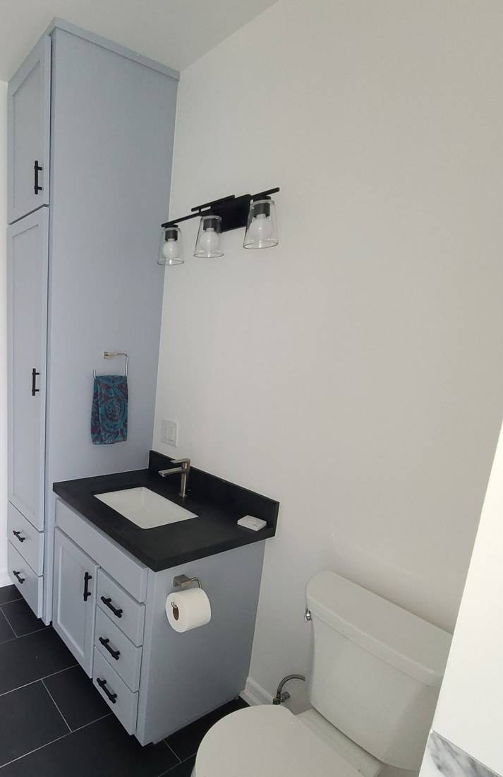 A blue-gray Shaker vanity with a black top beside a matching linen tower reaching the ceiling