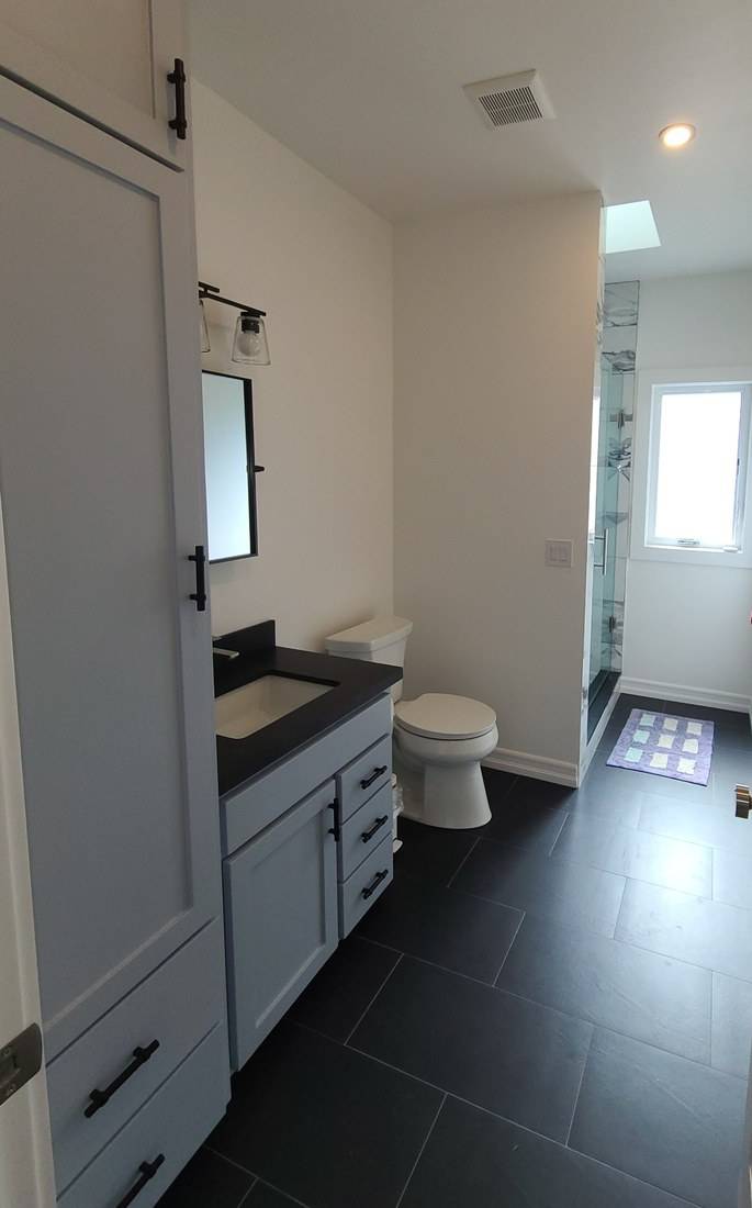 A blue-gray Shaker linen tower and vanity along one wall of a bathroom with a dark tile floor