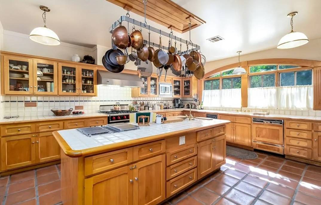 A large kitchen with warm wood cabinets, a tiled island and a wood pot rack hanging above it
