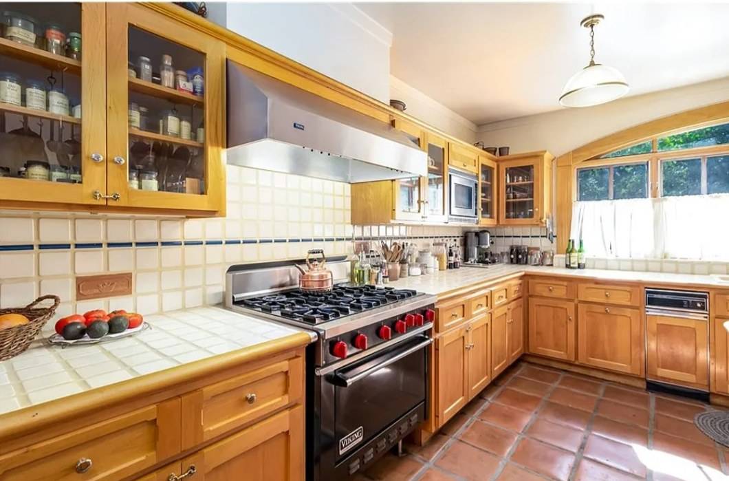 Warm wood wall cabinets with glass doors beside a range and hood