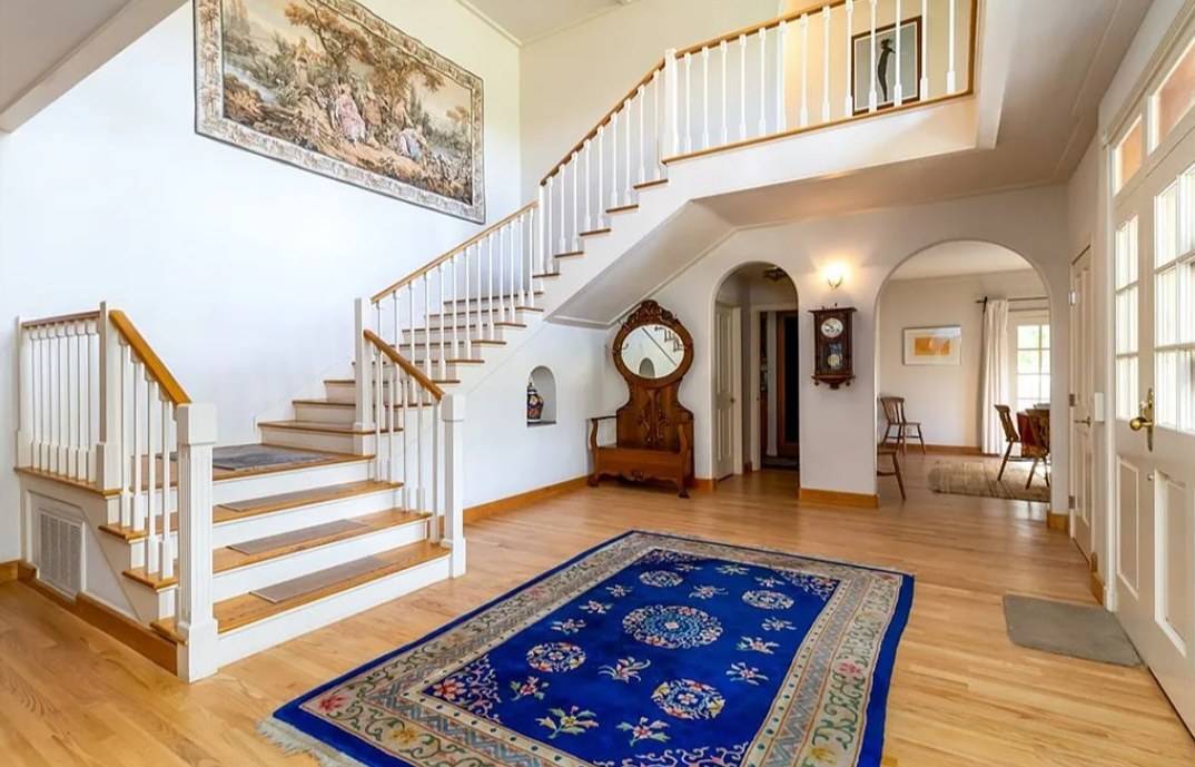 A stair with wood treads and a white railing of turned balusters rising to a gallery