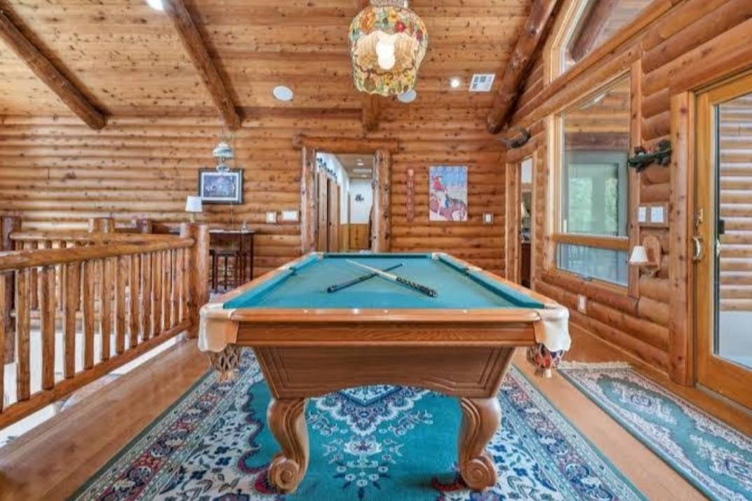 A loft game room with a wood railing of square balusters and a plank ceiling