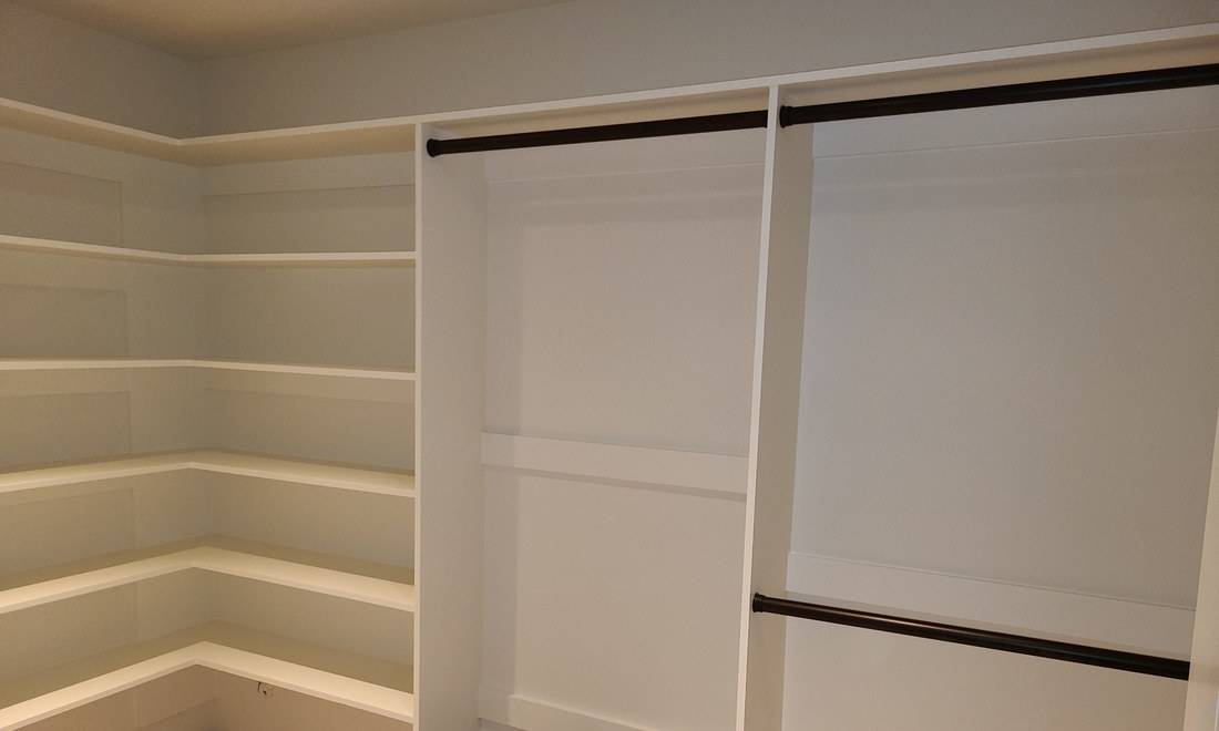 A painted white closet with five tiers of corner shelves and two bays of hanging rods