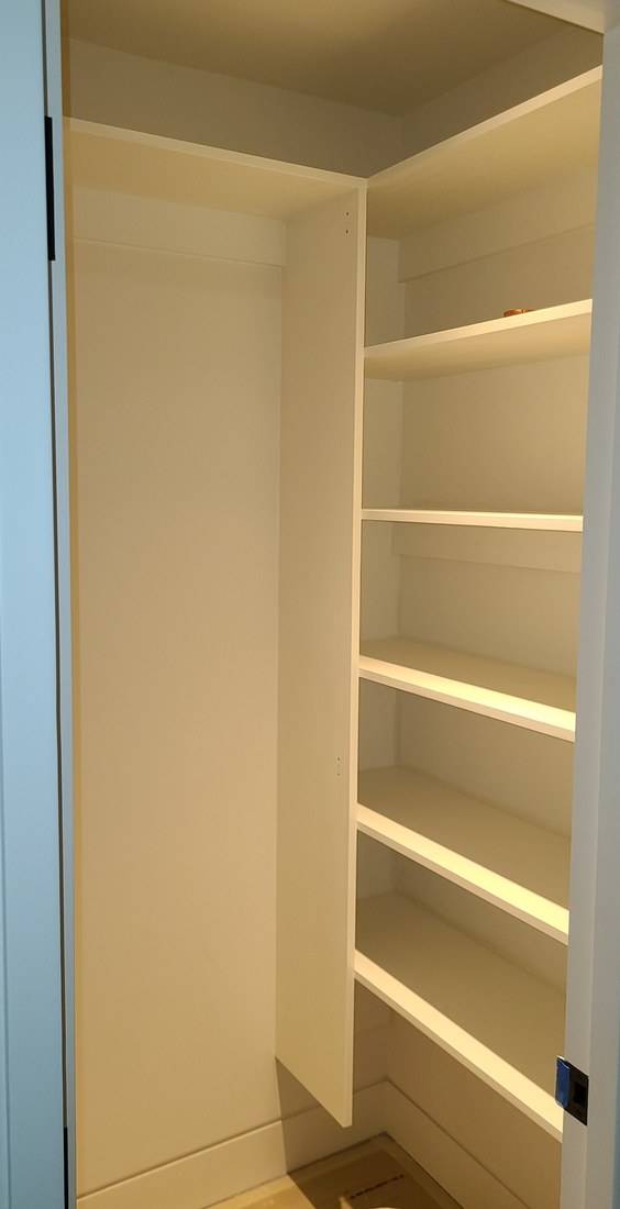 A small pantry with painted white shelves fitted between a side panel and the wall