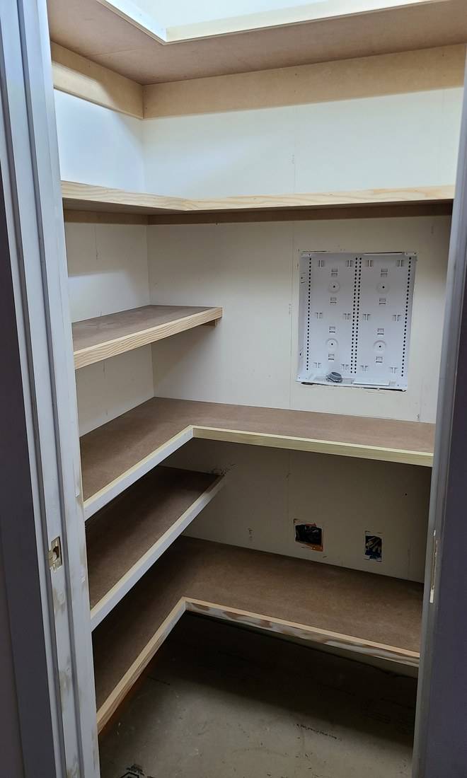 Unpainted pantry shelves wrapping a corner, each with a solid wood strip along its front edge