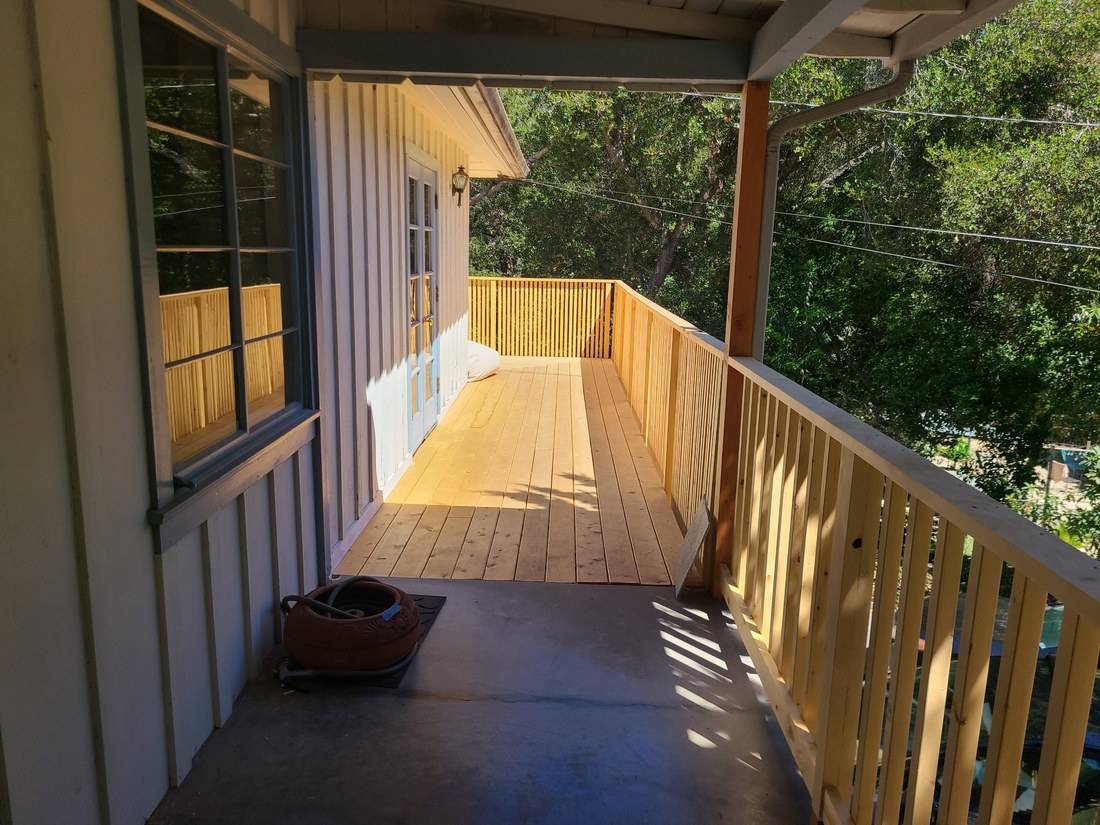 A new wood deck with a railing of closely spaced vertical balusters along a board-and-batten house