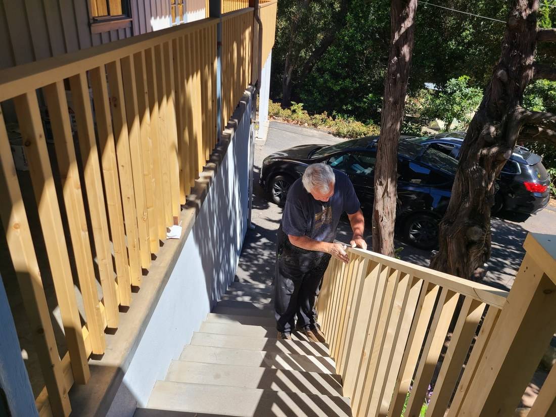 Tom, a white-haired carpenter, sanding the top of a new wood stair railing