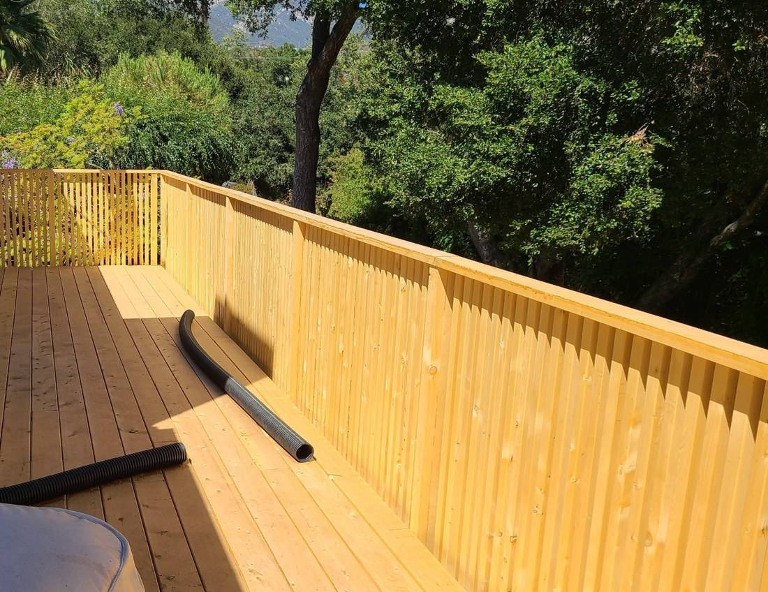 New deck boards running to a solid-looking guard rail of vertical balusters, with trees beyond
