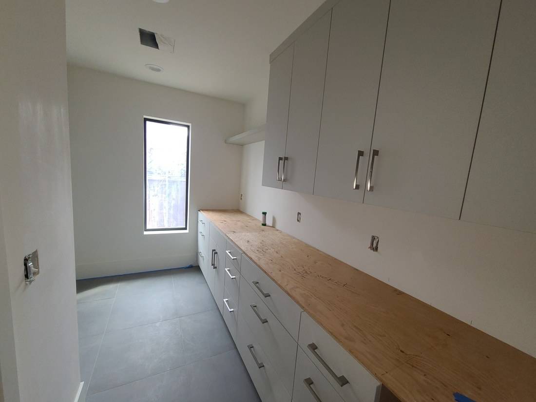 A long run of pale flat-panel drawers and wall cabinets in a laundry room