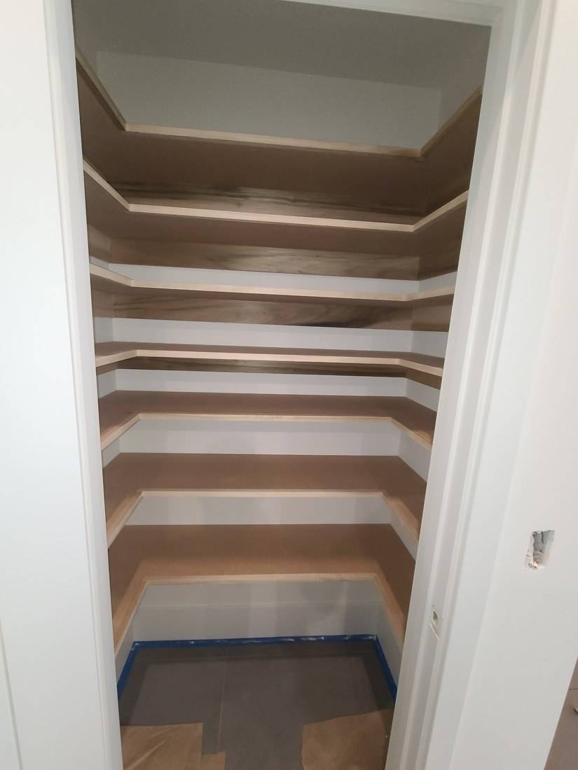 A closet pantry with seven tiers of U-shaped shelves edged in solid wood