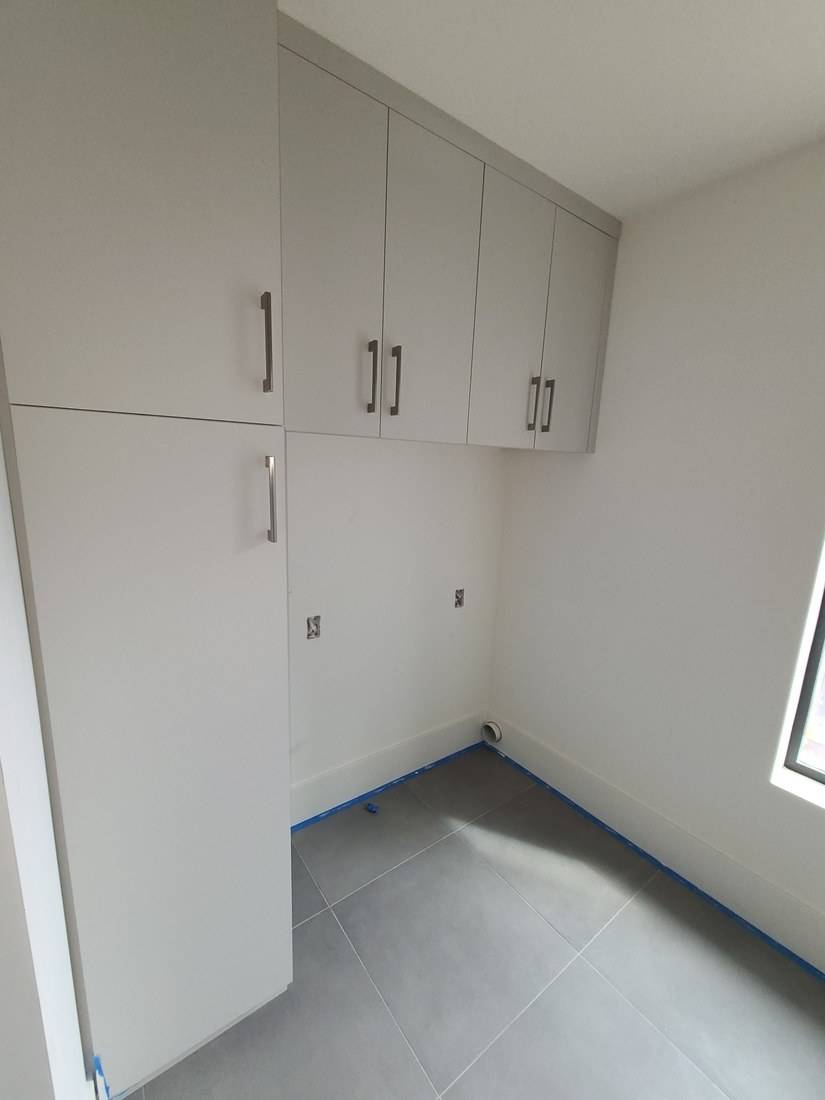 Pale flat-panel tall and upper cabinets fitted tight to the ceiling and wall