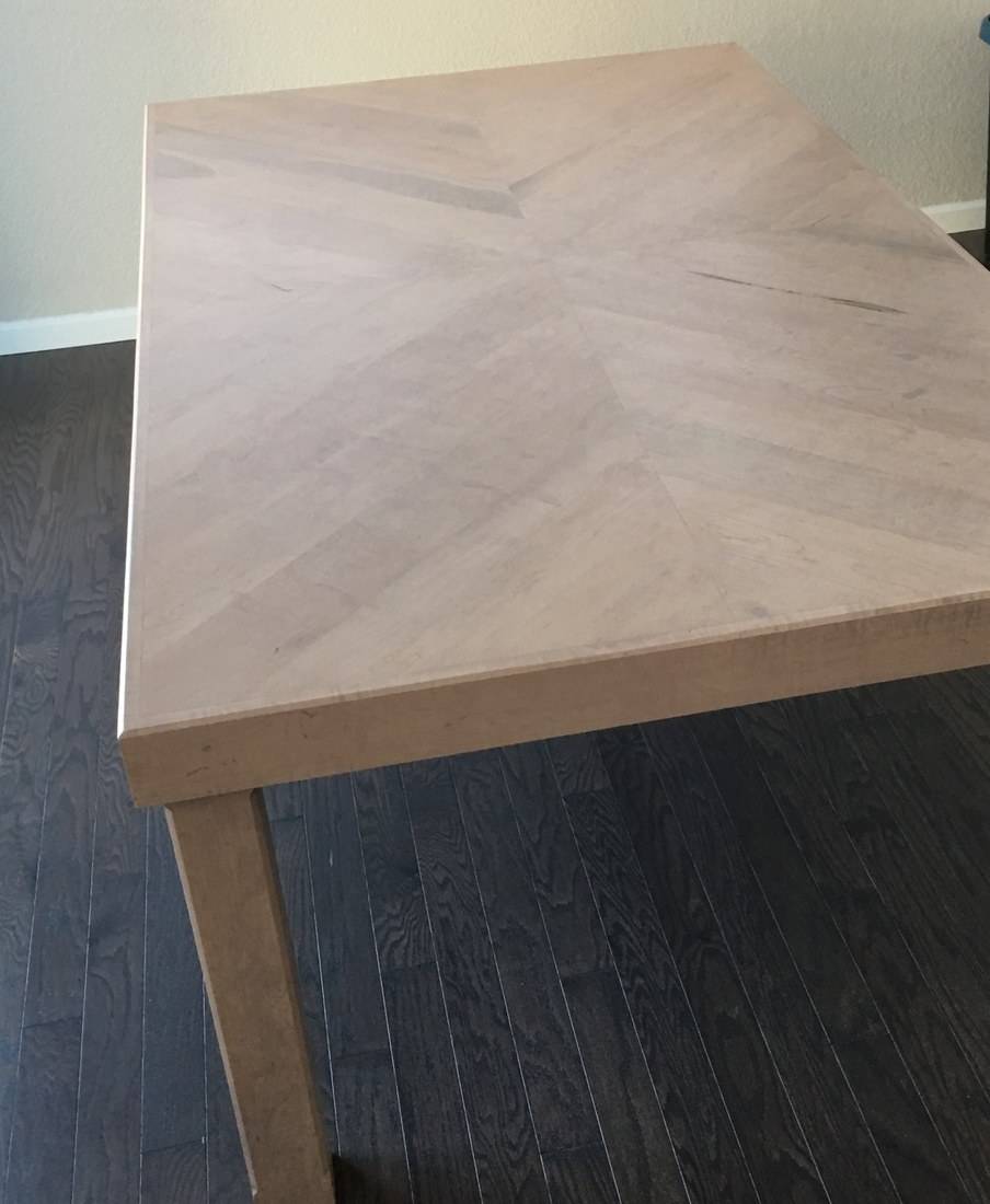 A large maple dining table with a chevron-pattern top on square legs