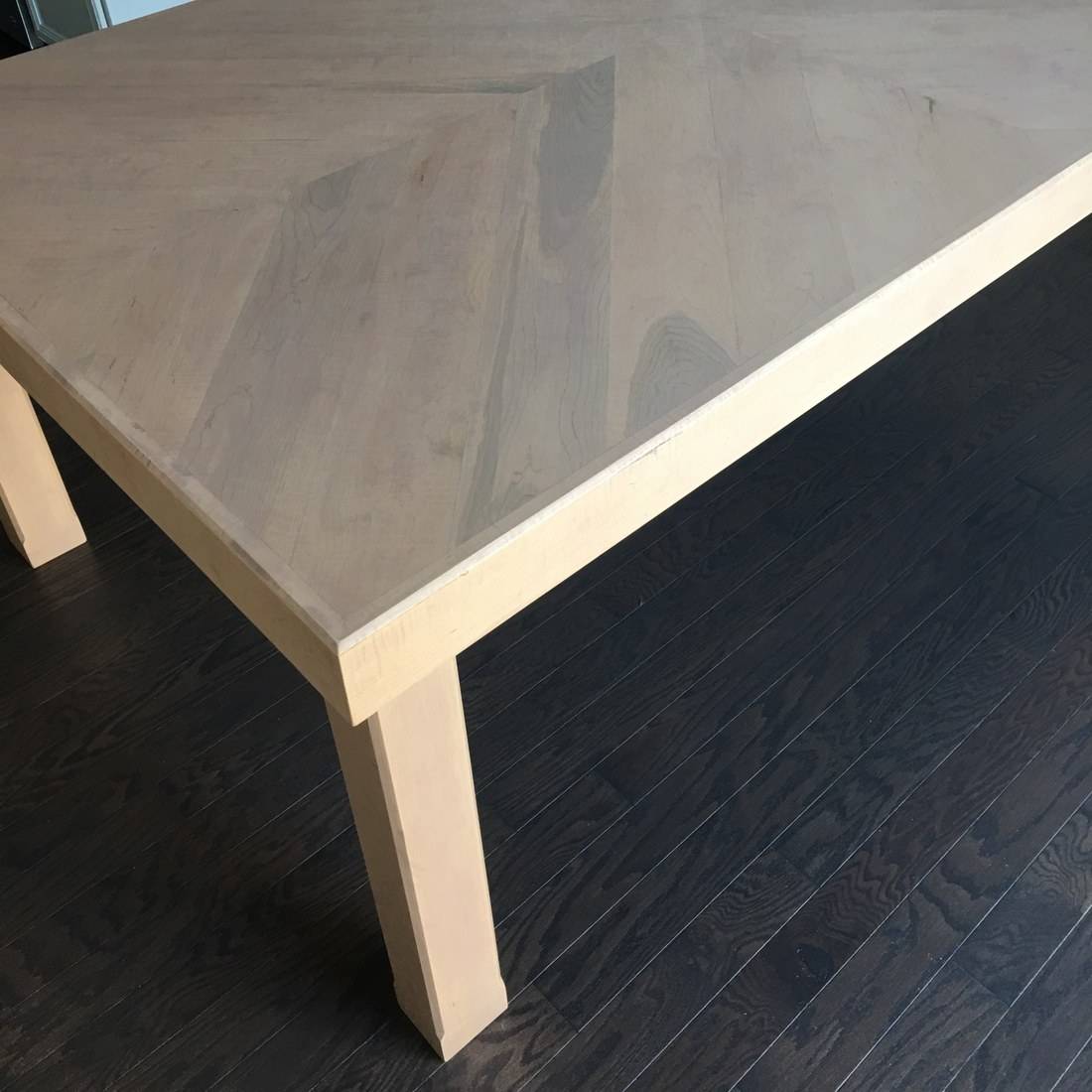 The corner of a maple table showing the mitered border around a chevron top, the apron and a square leg