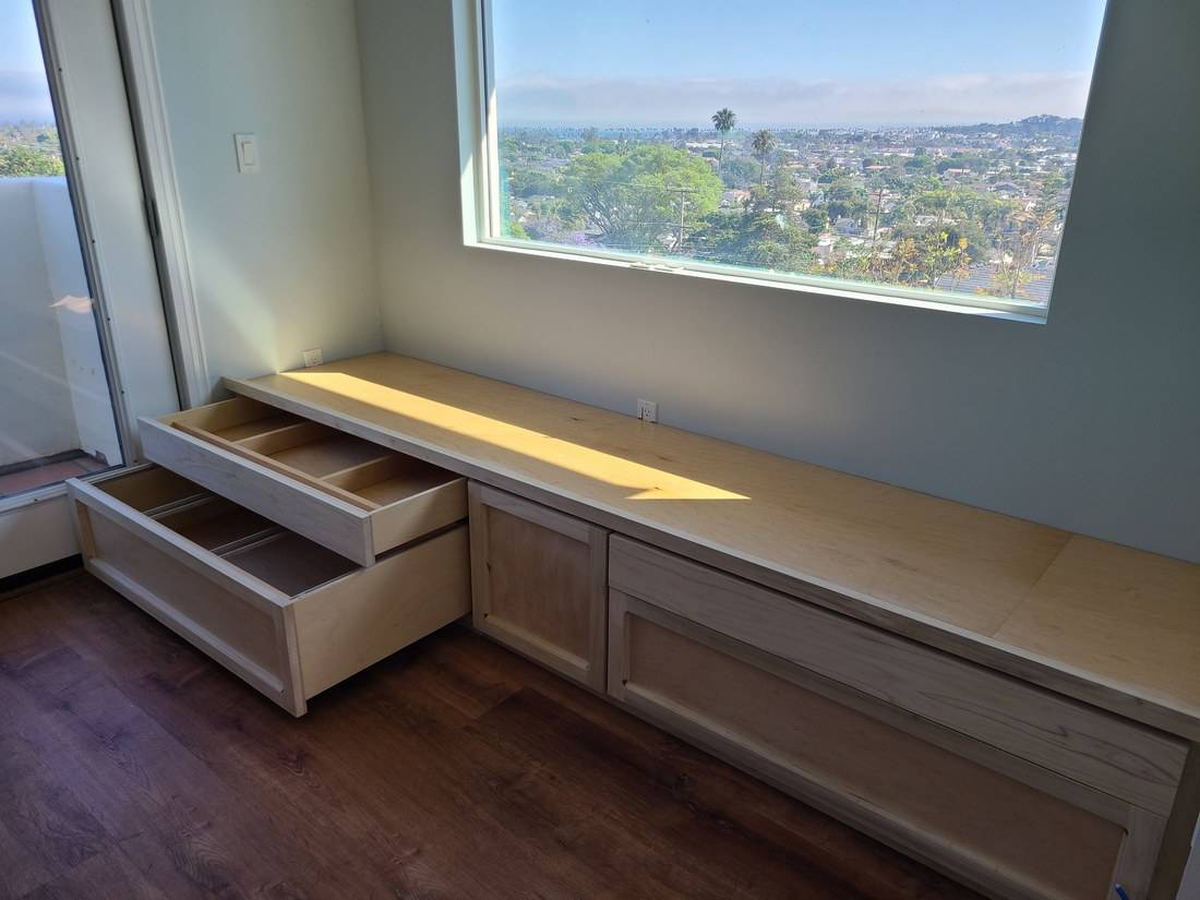 A maple window seat under a large window, with a deep drawer and a divided tray pulled open