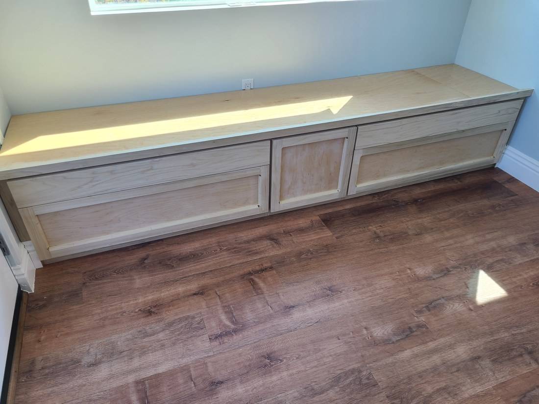 A long maple window seat with frame-and-panel drawer fronts fitted between two walls