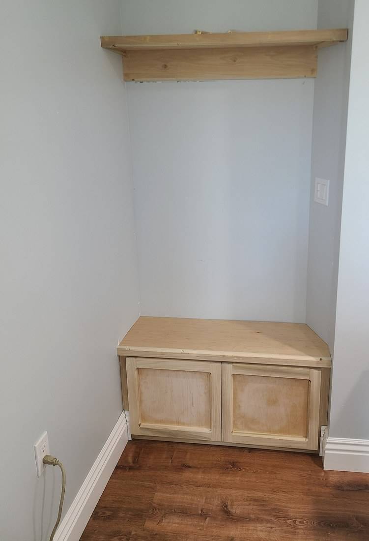 A maple storage bench with two panel doors and a shelf above, fitted into an alcove beside a front door