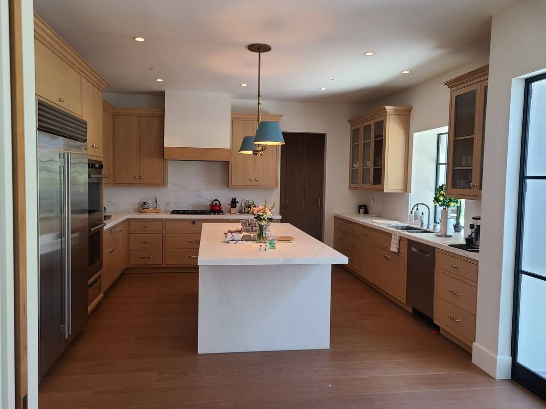 A kitchen with pale oak frame-and-panel cabinets, a paneled hood, glass-fronted wall cabinets and a white stone island