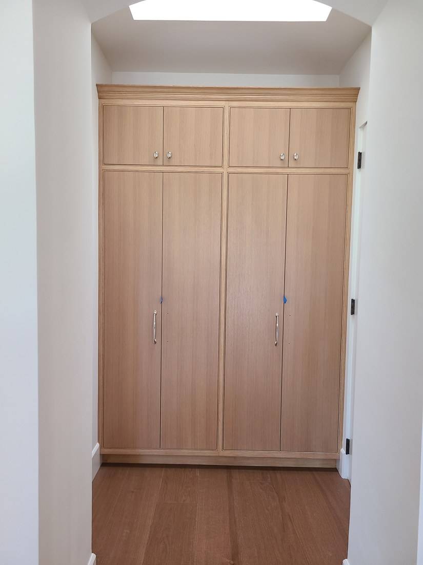 A floor-to-ceiling pale oak cabinet with four tall doors and four upper doors, fitted into a hall alcove