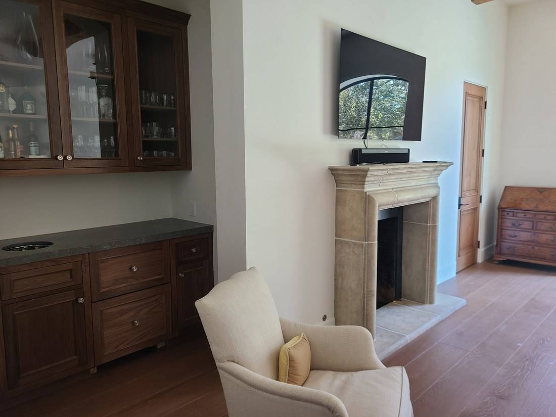 A dark wood bar cabinet with glass-fronted upper doors and drawers below, beside a stone fireplace