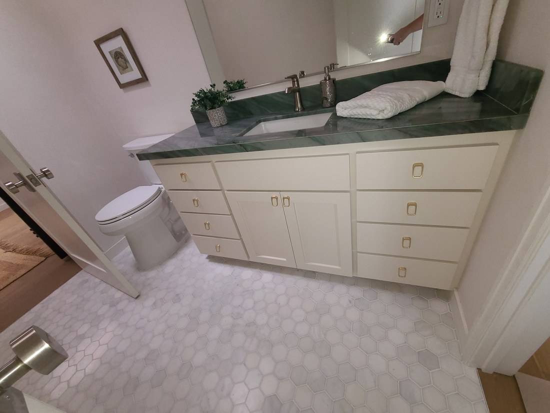 A cream painted Shaker vanity with brass pulls under a green stone top