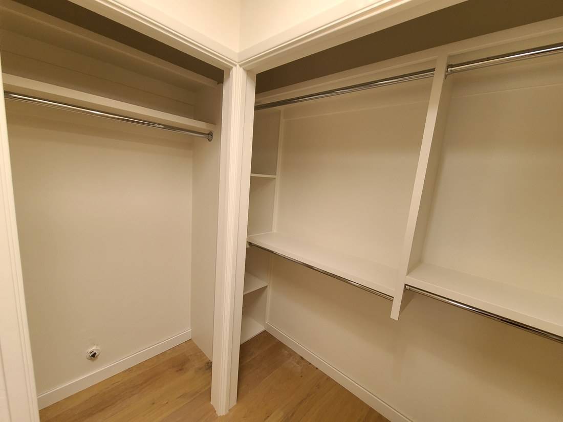 A painted white closet with shelves and hanging rods on three walls