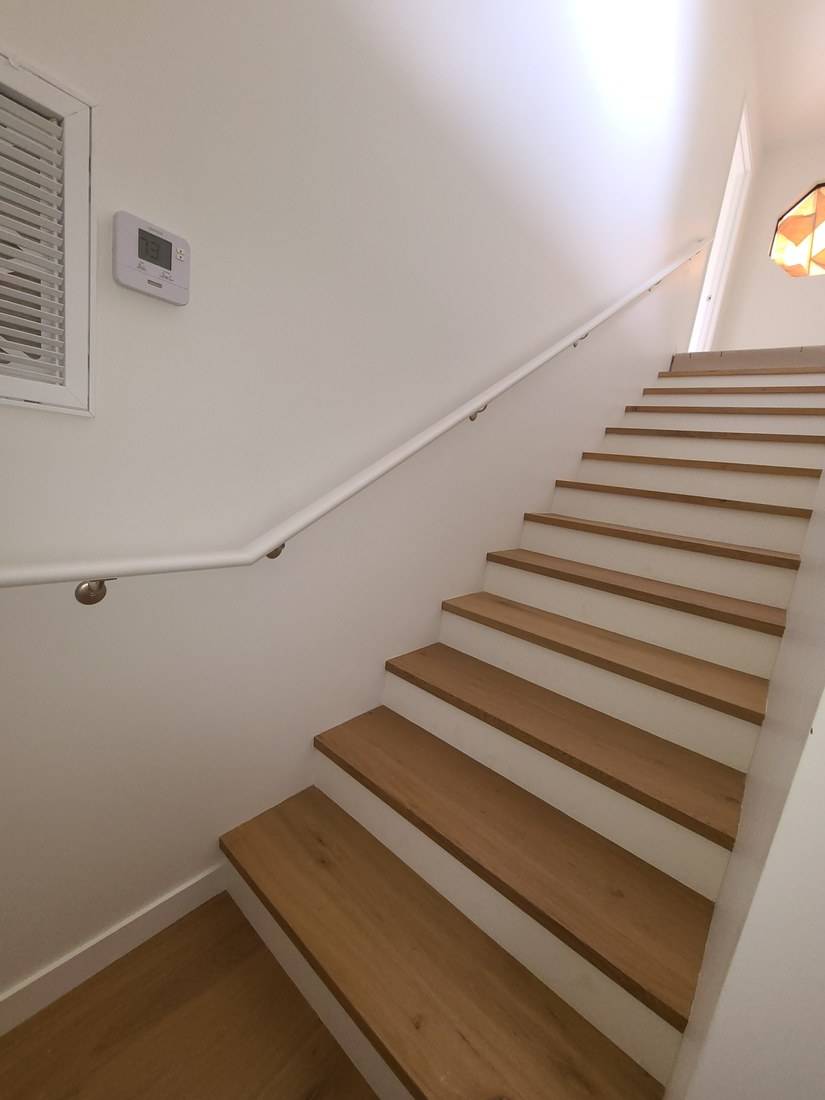 A stair with new light wood treads, white risers and a wall-mounted handrail