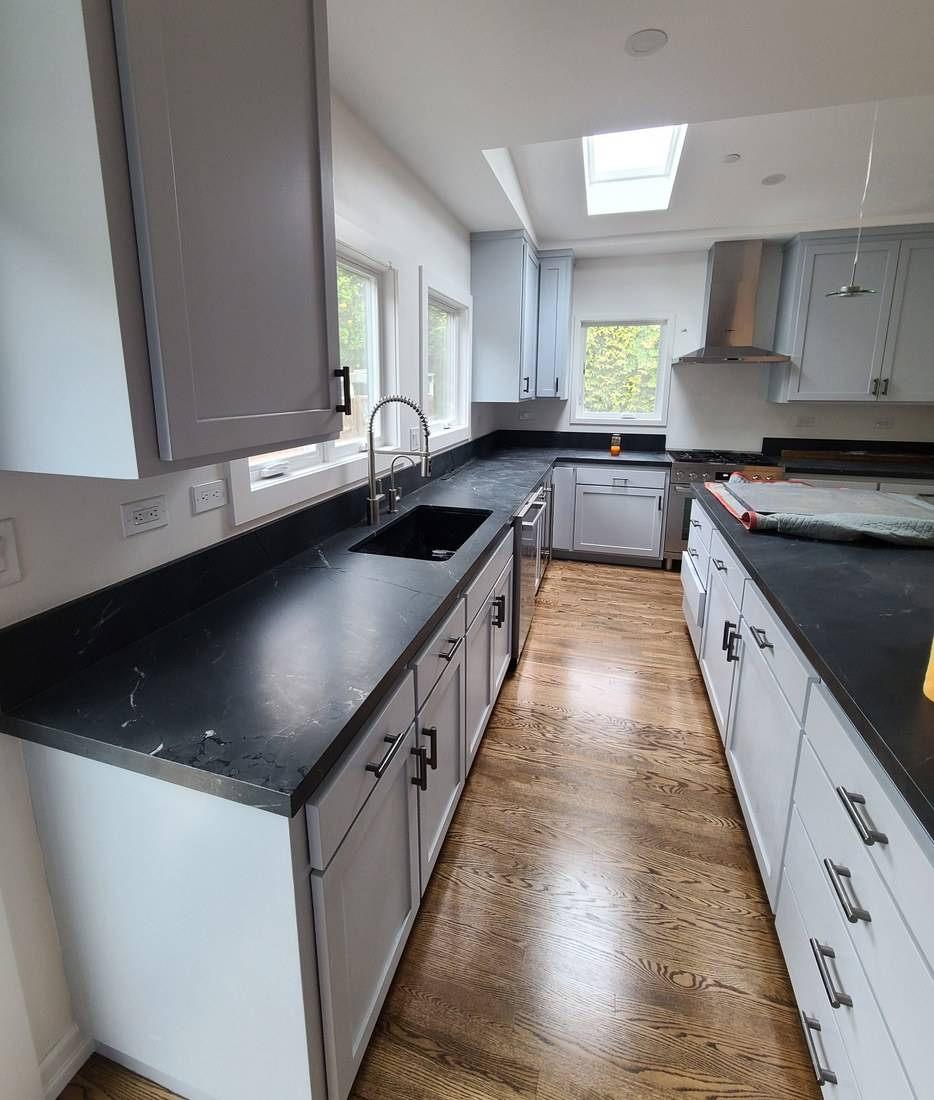 A kitchen with blue-gray Shaker cabinets, black stone counters, black pulls and an oak floor