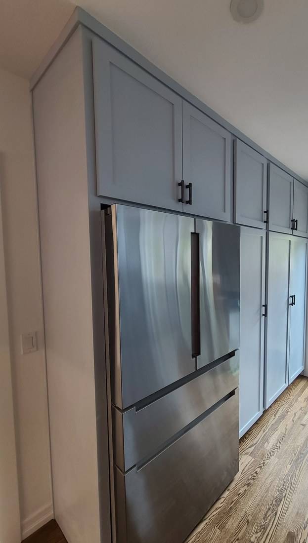 A full-height wall of blue-gray Shaker cabinets surrounding a stainless refrigerator