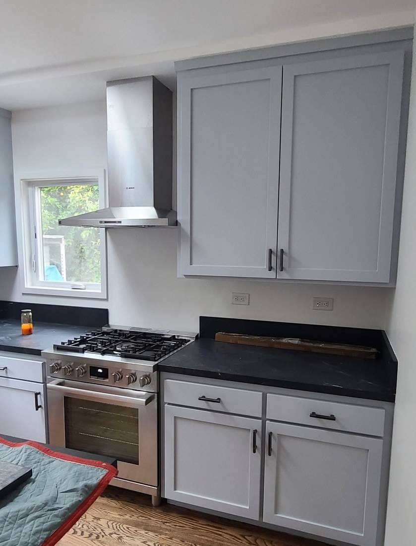 Blue-gray Shaker base and wall cabinets on either side of a stainless range and hood