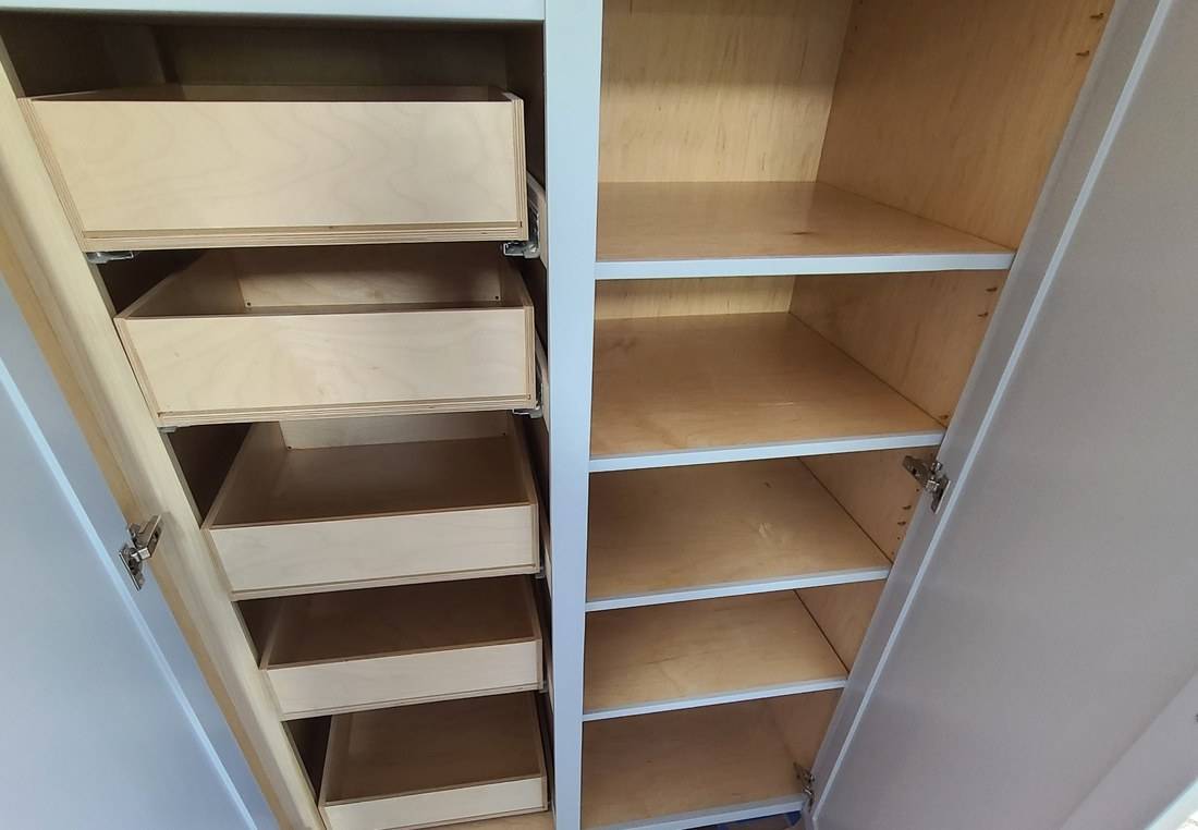 An open pantry cabinet showing five plywood pull-out trays on the left and adjustable shelves on the right