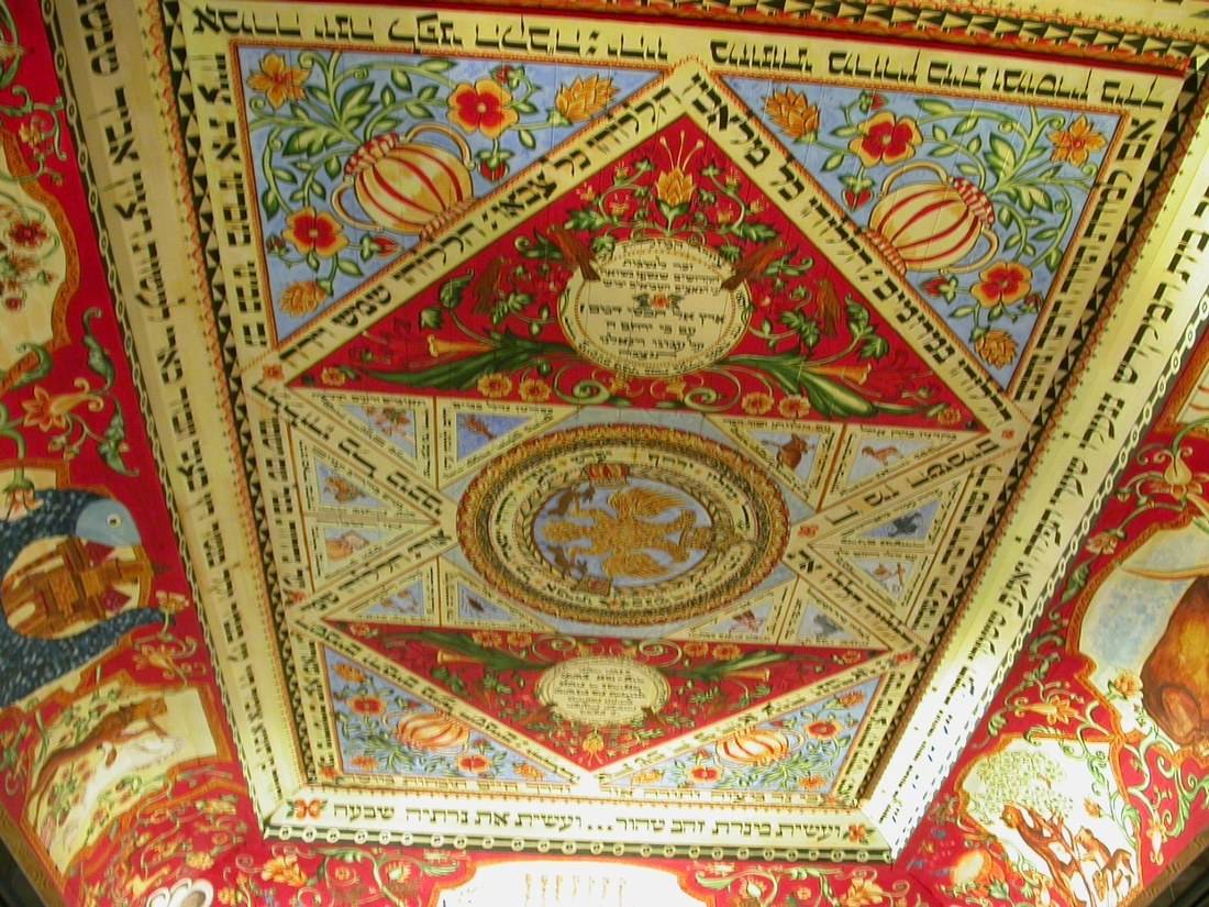 A richly painted wood ceiling of angled panels in red, blue and gold with Hebrew lettering