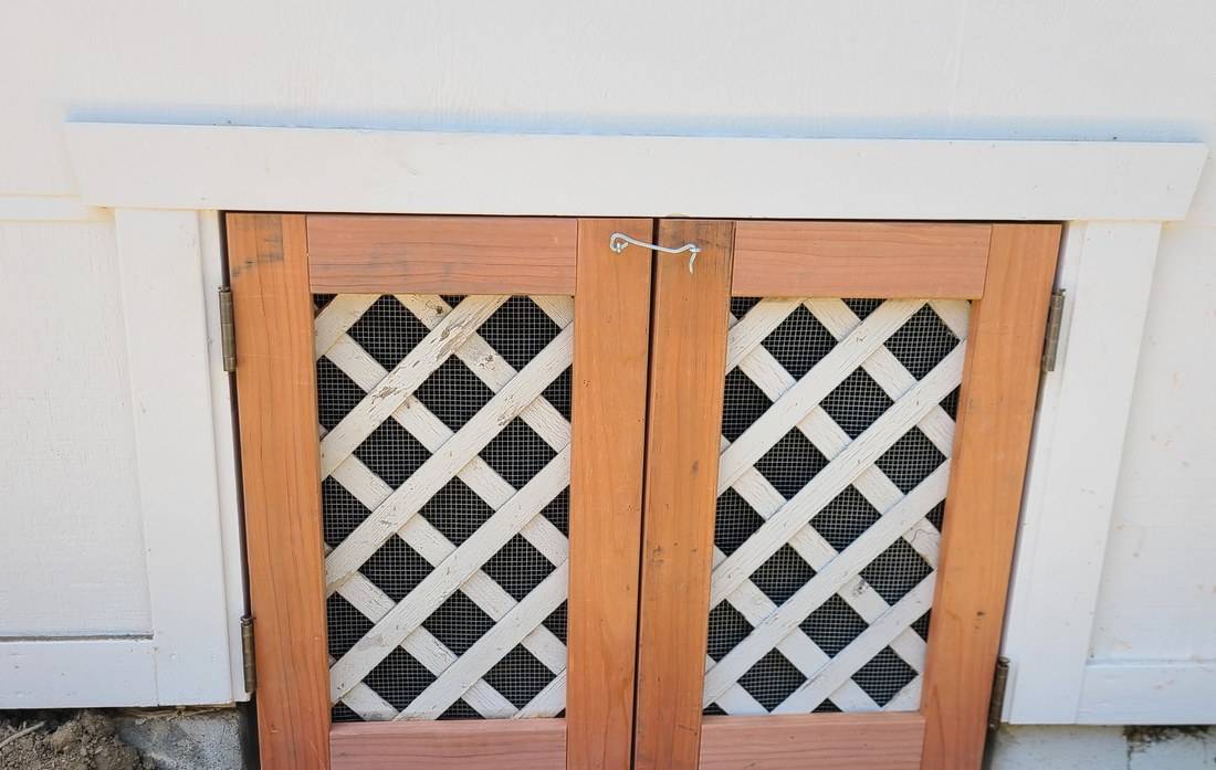 A pair of small redwood-framed doors with white lattice and screen set into white exterior trim
