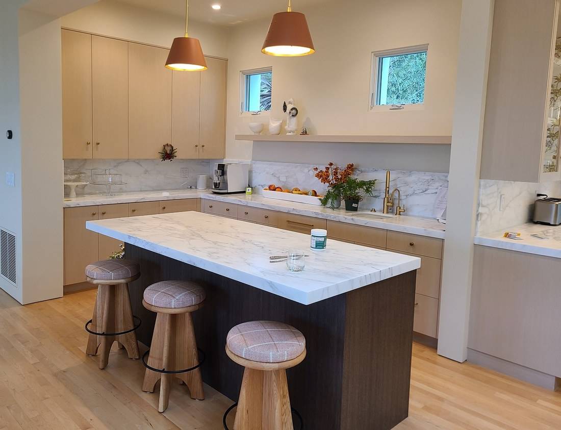 A kitchen with pale oak flat-panel cabinets, marble counters, a dark wood island and a long floating oak shelf