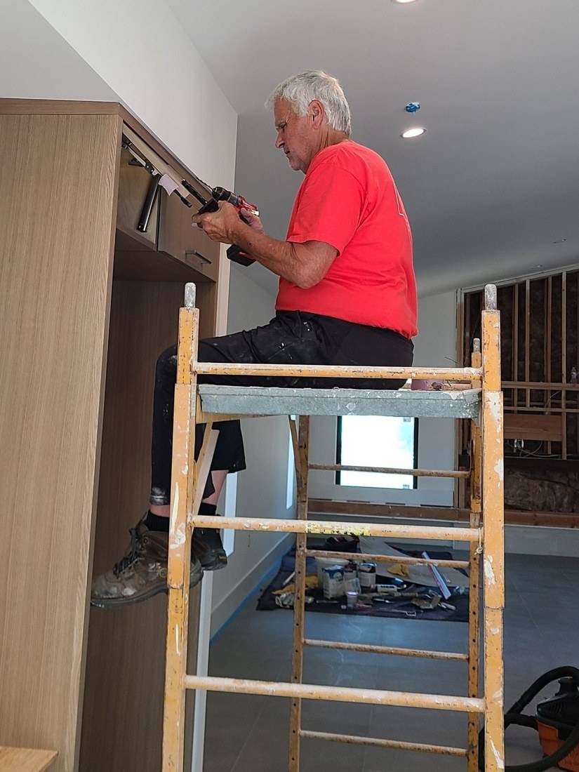Tom fitting cabinet hardware from a rolling scaffold
