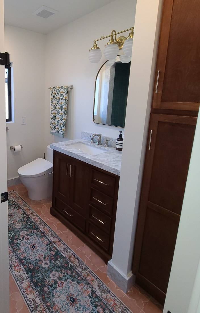 A dark stained wood vanity with drawers under a marble top, and a matching tall linen cabinet