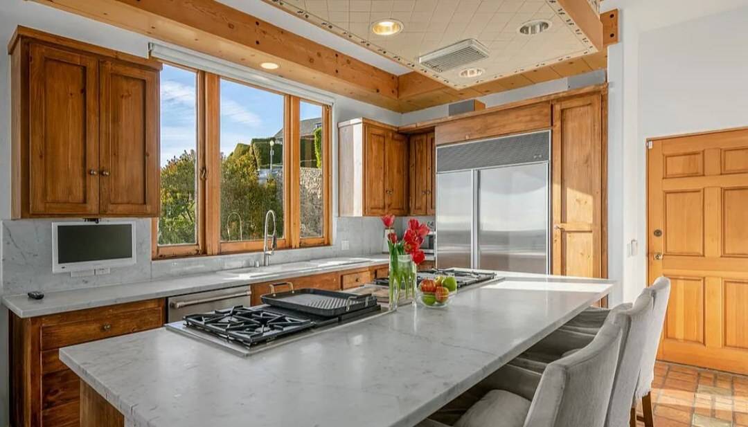 A kitchen with stained wood frame-and-panel cabinets, wood-cased windows and a marble island