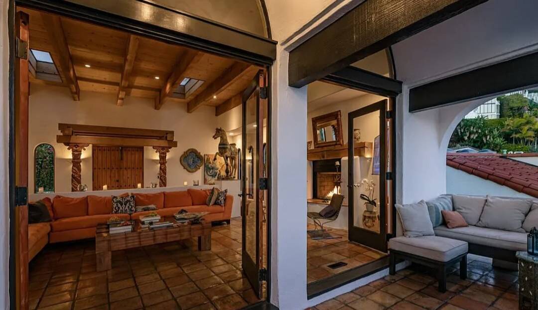 Tall wood-framed glass doors standing open between a beamed living room and a tiled terrace