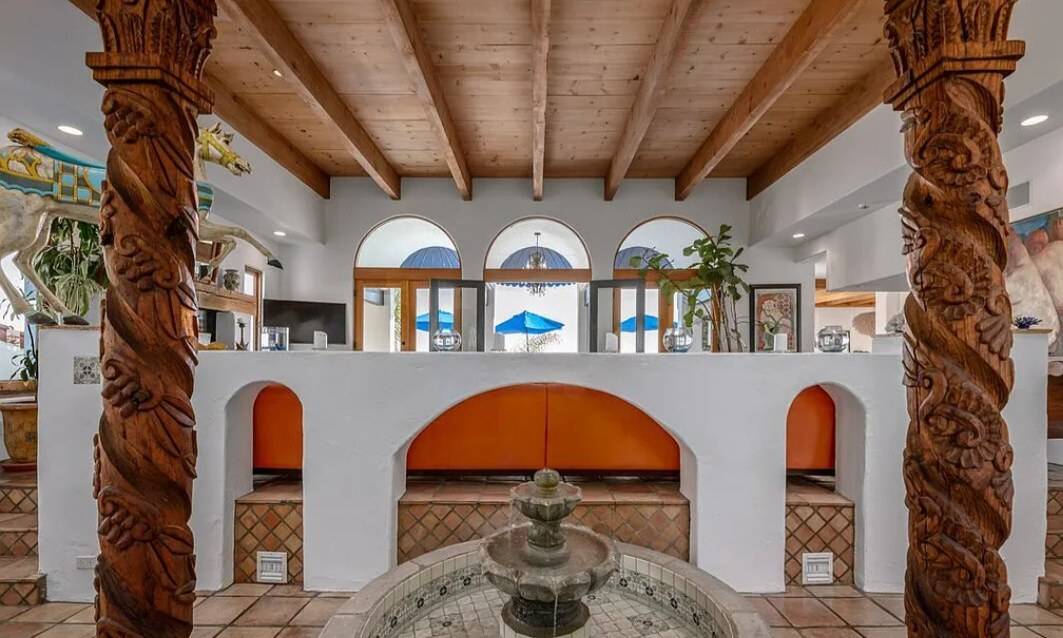 Exposed wood beams and a plank ceiling above white plaster walls with arched openings