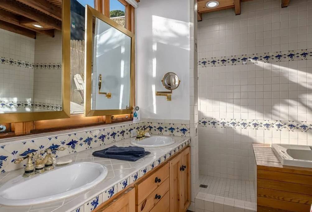 A wood vanity with drawers and doors under a tiled counter with two basins, and wood-framed mirrors above