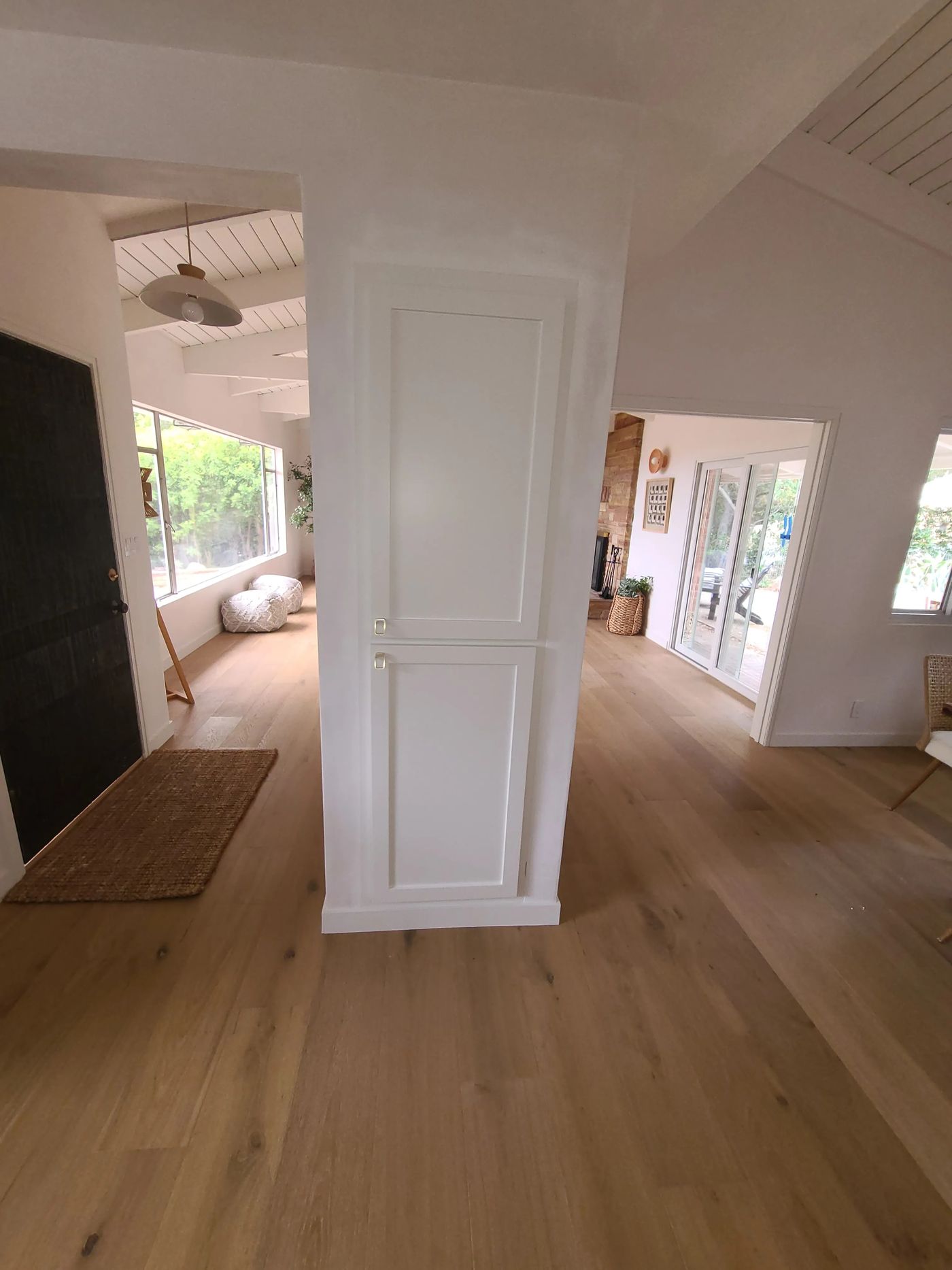 A white paneled built-in cabinet set into a wall between two openings, with the dark front door and entry hall on the left and the living room with its stone fireplace and sliding doors on the right