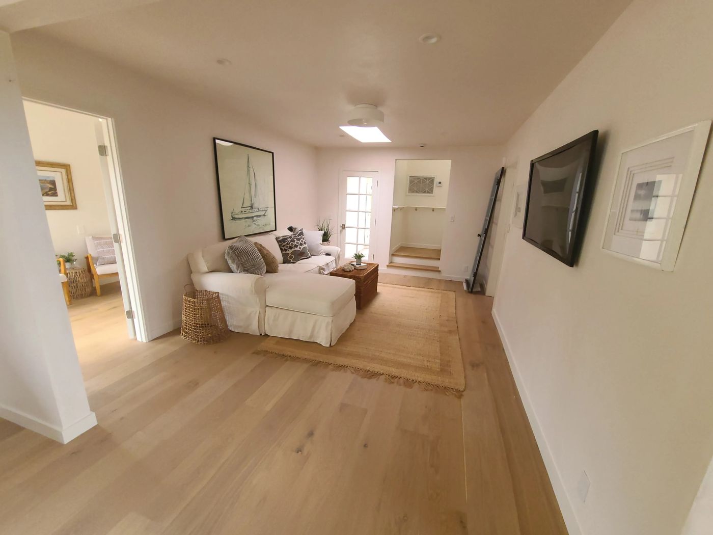 A family room with a skylight, a glass-paned door to the garden, steps up to a landing, and wide-plank wood floors, with a bedroom visible through a door on the left