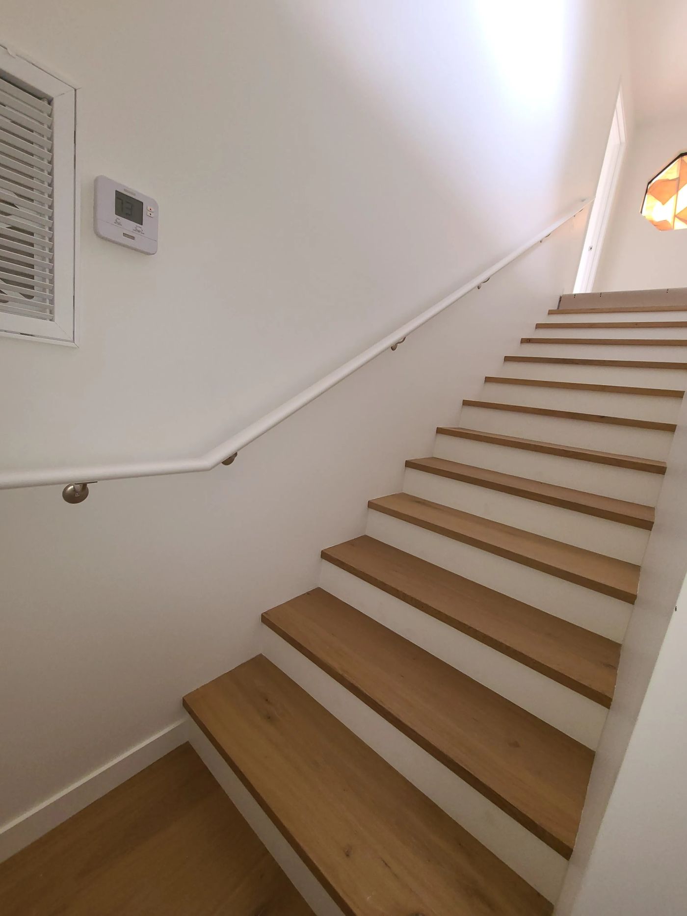 A straight stair with wood treads matching the floors, white risers and a white wall-mounted handrail